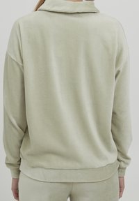 Felpa in corduroy verde chiaro con colletto, caratterizzata da una vestibilità rilassata, texture a costine e polsini elasticizzati. Nessun marchio o motivo visibile.