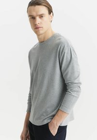 Szara longsleeve koszulka z okrągłym dekoltem, wykonana z miękkiego materiału. Krój jest luźny, a koszulka ma subtelne detale przeszyć.