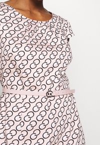 Robe rose avec un motif circulaire noir et blanc, manches courtes, détail plissé au niveau de l'encolure, et une fine ceinture avec une boucle circulaire.