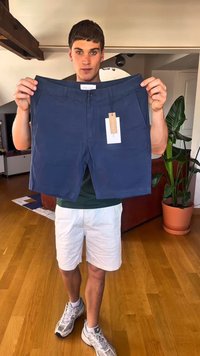 Tummansinisen väriset kevytkangasta shortsit, joissa on nappi- ja vetoketjusuljenta, kiinnitetty lappu ja siisti muotoilu.