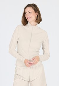 Helle beige Zip-Up-Jacke aus glatter Stoffqualität, mit langen Ärmeln und Stehkragen. Kombiniert mit passenden, lockeren Hosen.