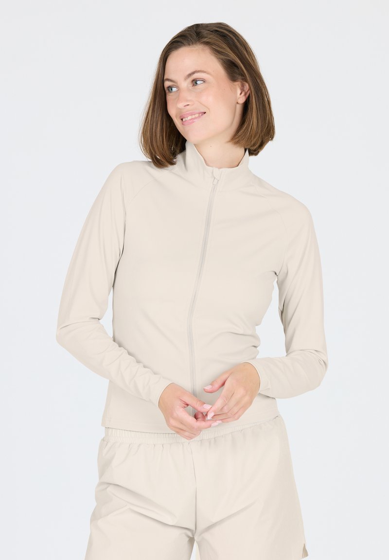 Helle beige Zip-Up-Jacke aus glatter Stoffqualität, mit langen Ärmeln und Stehkragen. Kombiniert mit passenden, lockeren Hosen.