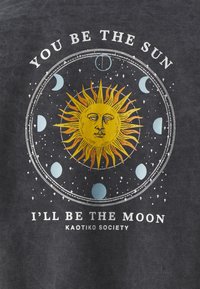 Gul sol med ansikte omgiven av måncykler i en cirkulär design med texten "DU VAR SOLEN, JAG BLIR MÅNEN" på mörk tyg.