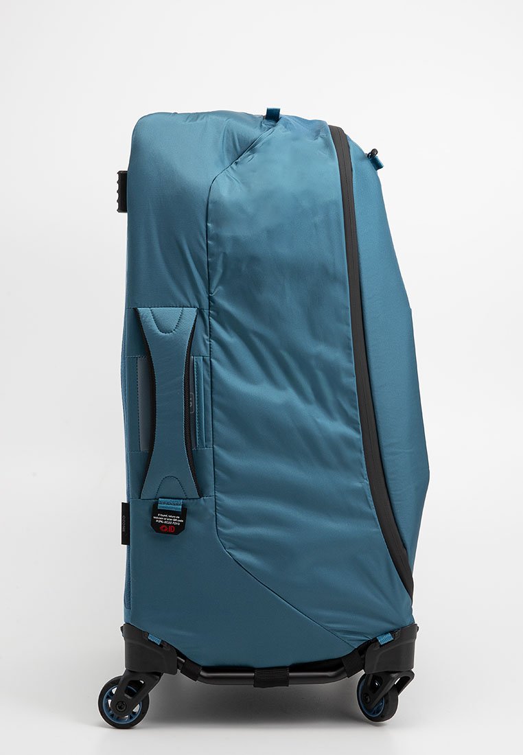 Maleta azul rodante hecha de tejido texturizado, con un asa lateral, cremallera y ruedas duraderas para un fácil transporte.