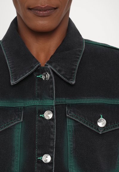 Veste en denim noir avec des accents verts, présentant un col classique, des boutons en métal argenté et des coutures contrastées. Détails de poches remarquables.