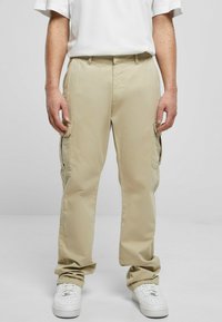 Pantalones cargo beige con múltiples bolsillos laterales, hechos de una tela ligera. Diseño de pierna ajustada, combinados con zapatillas blancas.