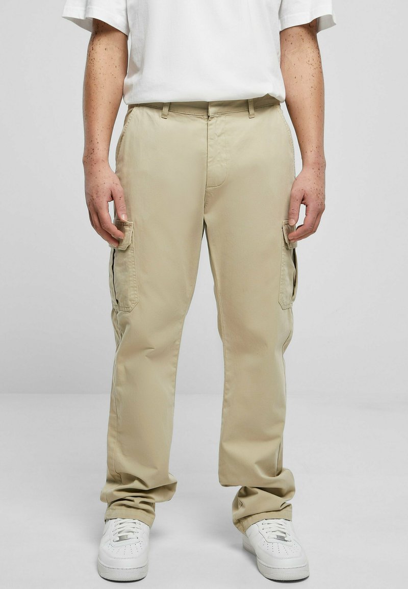 Pantalones cargo beige con múltiples bolsillos laterales, hechos de una tela ligera. Diseño de pierna ajustada, combinados con zapatillas blancas.