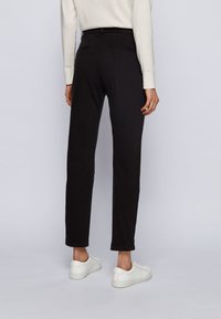 Pantalones negros ajustados con una textura suave, que cuentan con dos bolsillos traseros, dobladillos remangados y se combinan con zapatillas blancas.