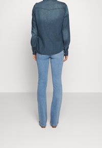 Denim shirt in dark blue with a classic collar, long sleeves, and buttoned cuffs, paired with light blue flared jeans featuring a slight wash.