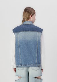Denim vest with a light blue body and dark blue dotted shoulders. Features a raw edge and no sleeves, showcasing a simple design.