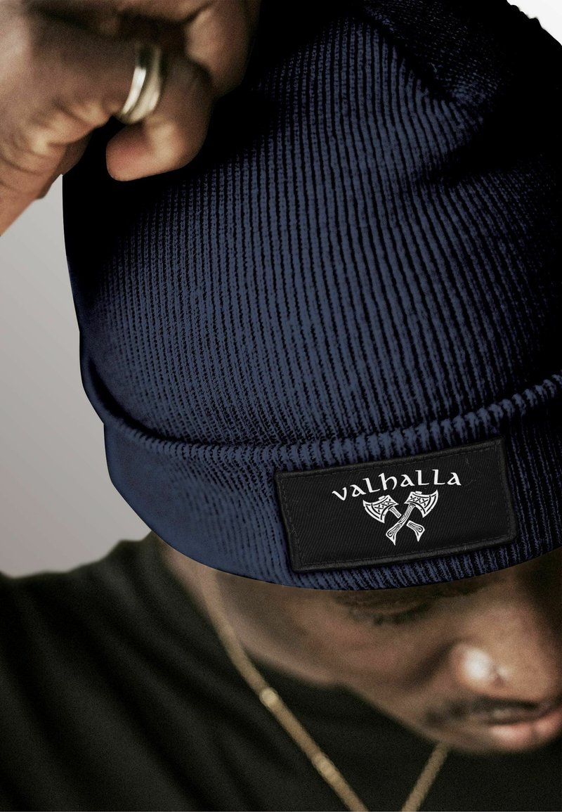 Navy blue knitted beanie with a ribbed texture and a black label featuring the text "valhalla" and axe graphics on the front.