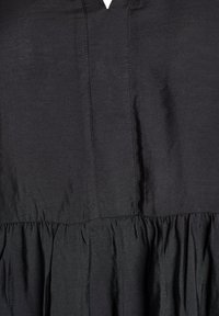 Must mustriga, millel on tekstureeritud viimistlus, koos kokkutõmmatud seeliku ja õrnade õmbluse detailidega rinnaosas. Nähtavat riistvara või mustreid pole.