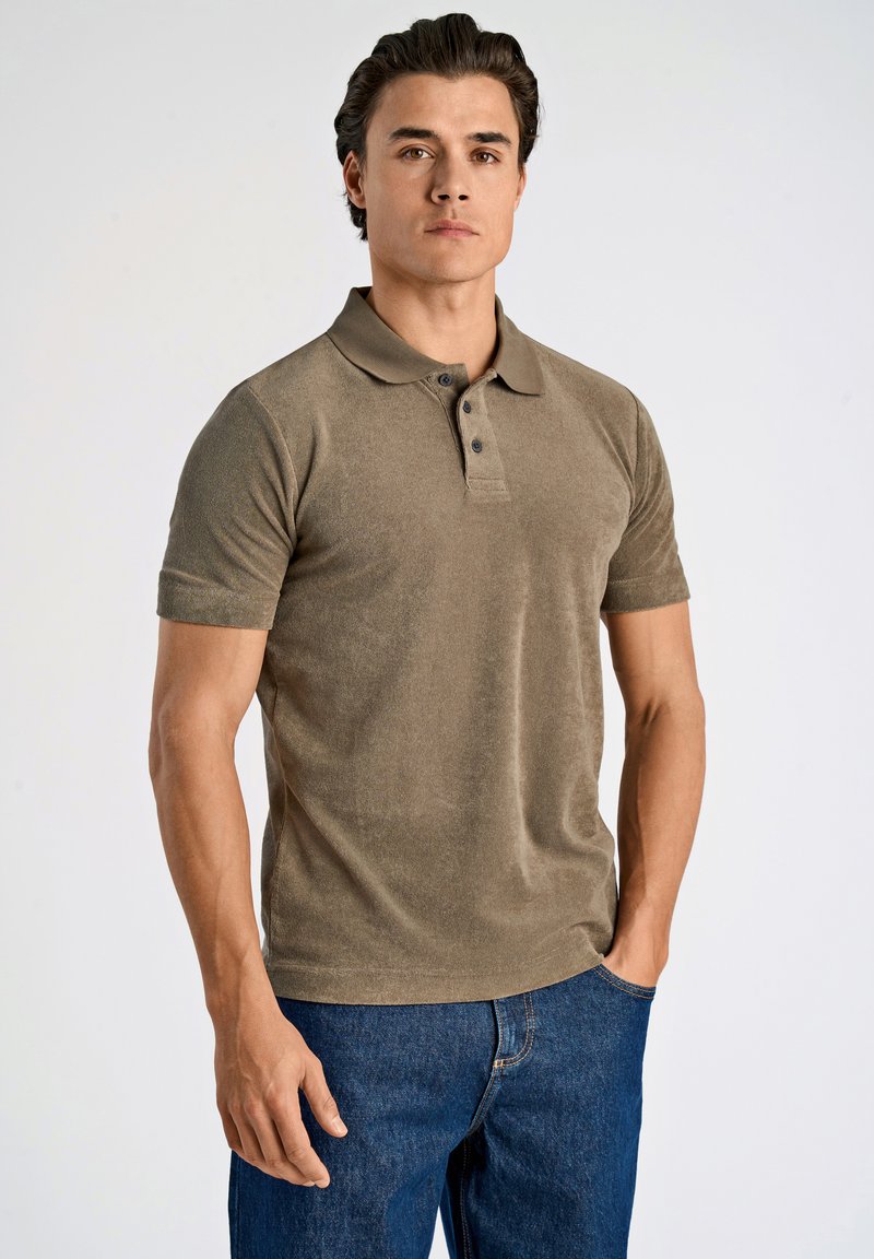 Polo in khaki con una texture morbida, colletto a tre bottoni e maniche corte. Indossato con jeans blu scuro. Design semplice e casual.