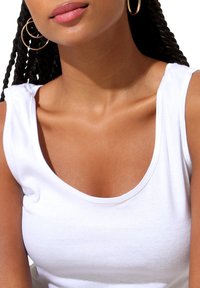 White sleeveless tank top with a scoop neckline, made from a soft cotton blend. Features a smooth texture and fitted silhouette.
