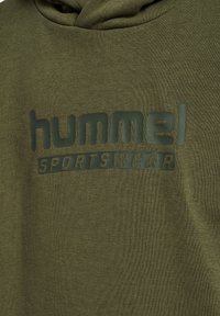 Tissu vert olive avec logo noir embossé "hummel SPORTSWEAR" sur un vêtement de sport.