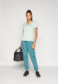 Μέντα πράσινο T-shirt με V-λαιμόκοψη, σε συνδυασμό με τζελ jogging σε τιρκουάζ, μαύρα αθλητικά παπούτσια και μαύρη τσάντα duffel. Λείο ύφασμα, άνετη εφαρμογή.