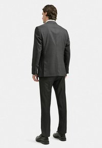 Kolgrå skräddarsydd kavaj med en enda slits bak, tillsammans med matchande byxor och svarta snörskor, slät tygtextur.