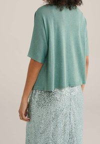 Krátký rukáv, světle tyrkysový top z texturované, třpytivé látky, doplněný lesklou světle modrou sukní s flitry.