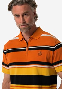 Polo triko oranžové barvy s horizontálními černými, bílými a žlutými pruhy, s polo zipem a kulatým logem na hrudi.