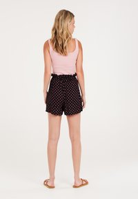 Pantaloni corti neri con un motivo a diamante rosa, vita elastica con dettaglio arricciato, abbinati a una canotta rosa chiaro e sandali piatti.