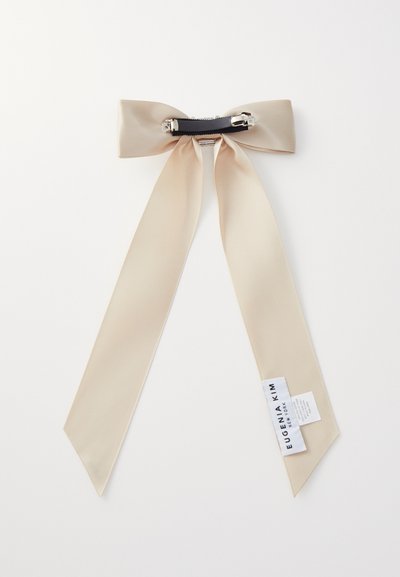 Vaalean beige satiininen nauha, jossa on pitkät hännät, musta keskibandi, jossa on hopeiset yksityiskohdat, ja etiketti yhdessä hännässä, joka osoittaa brändin.