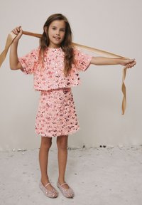 Pink sequined two-piece outfit with a cropped top and a matching skirt. Satin ribbon accents and sparkly flat shoes complete the look.