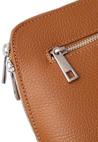 Brązowa skórzana saszetka na zamek z teksturowaną powierzchnią, wyposażona w metalowy suwak w kolorze srebrnym oraz staranne przeszycia wzdłuż brzegów.