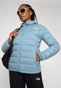 Light blue puffer jacket with quilting, high collar, and front zipper; features logo on the chest and 800 fill power detail on the sleeve.