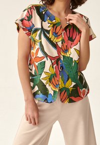 Chemise à manches courtes en tissu léger arborant un motif floral tropical aux couleurs vives, avec un devant à boutons et un ourlet arrondi.