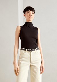 Must mustriga turtleneck, millega on koos kõrge vöökoha ja kreemivärvi püksid, kus on peen must vöö. Lihtne ja kaasaegne disain ribatekstuuriga.