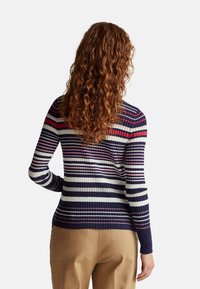 Pruhovaný svetr s žebrovanou texturou, s horizontálními pruhy v námořnické modré, růžové a bílé barvě, dlouhými rukávy a přiléhavým střihem.