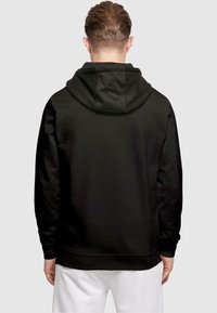 Mustaga kapuutsiga jakk, millel on suur, pehme kapuuts, soonilised mansetid ja ääred. Sile tekstuur ja minimalistik disain ilma nähtavate logode või mustriteta.