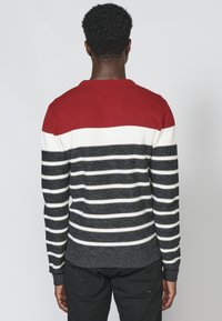 Maglione a righe rosse, bianche e blu navy con collo a giro e polsini a costine. Il materiale sembra essere lavorato a maglia con una texture liscia.