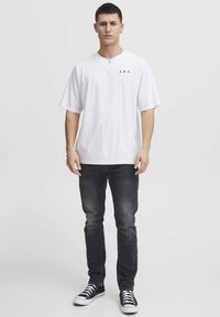 Hvid kortærmet t-shirt med "A.R.C." logo, parret med slim-fit mørke jeans og sorte low-top sneakers. Simpelt, afslappet design.