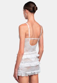Abito in pizzo bianco con un design trasparente e arricciato e spalline regolabili. Presenta un taglio sulla schiena e volant a strati all'orlo.