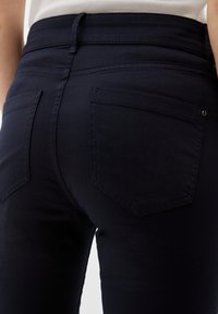 Pantalon en denim bleu marine foncé avec une coupe ajustée, comportant deux poches arrière et une surface lisse légèrement texturée.