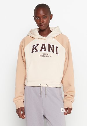 Hoodie corto in crema e beige con cordoncino, caratterizzato da una tasca a marsupio e testo stampato "KANI 1989 EST. BROOKLYN, NYC."