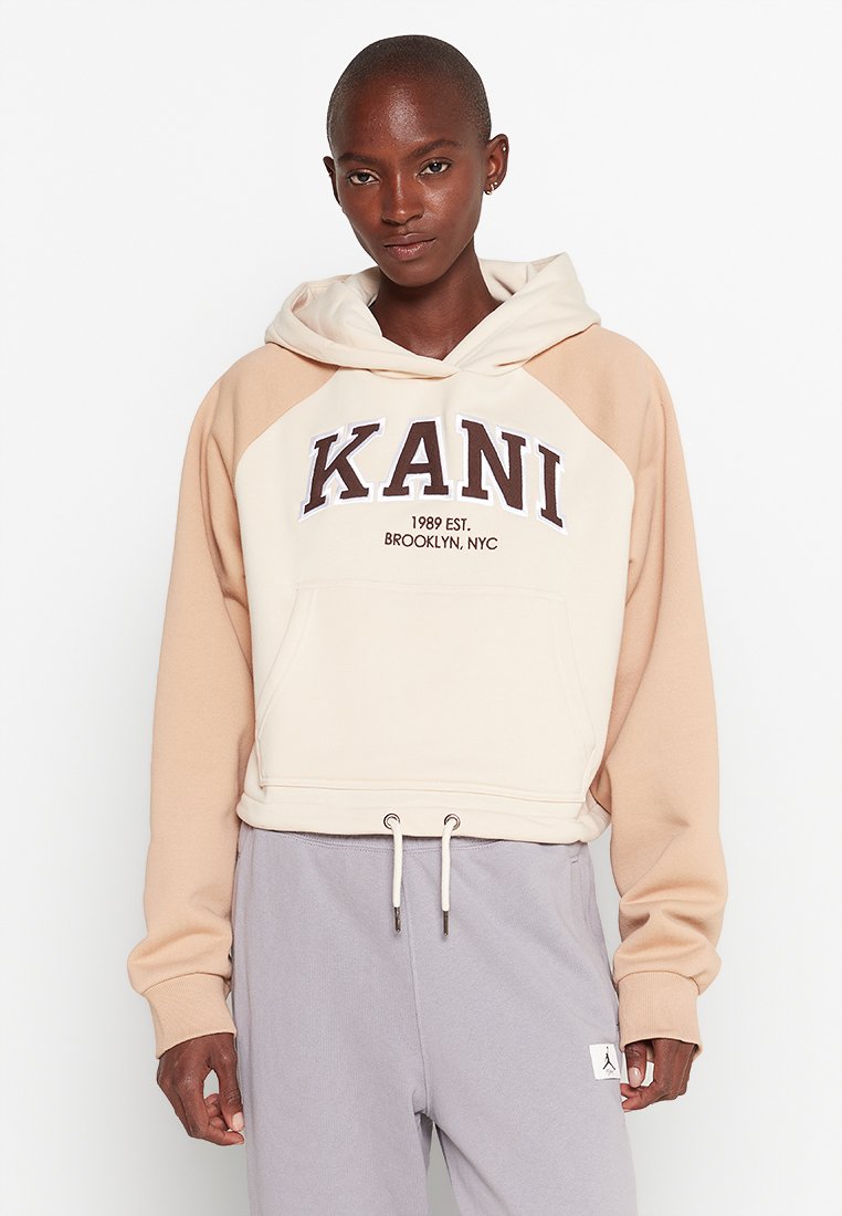 Hoodie corto in crema e beige con cordoncino, caratterizzato da una tasca a marsupio e testo stampato "KANI 1989 EST. BROOKLYN, NYC."