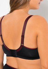 Černá podprsenka s červenými akcenty na ramínkách. Nastavitelná ramínka a zapínání na háček a oko na zadní straně, vyrobená z texturované látky.