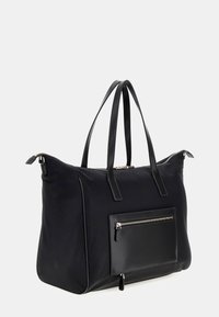 Zwarte nylon tote bag met een zachte textuur, dubbele handvatten en een voorvak met rits. Accentueert metalen hardware en contrasterende stiksels.