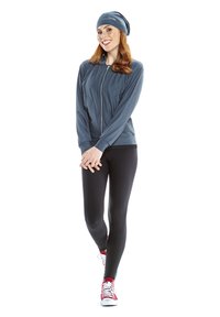 Gray athletic jacket with a full zipper, paired with black leggings and red sneakers. The model also wears a matching gray beanie.