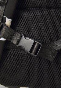 Black mesh fabric showing a buckle strap, featuring a textured surface with an adjustable nylon strap. No patterns or colors present.
