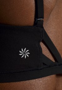 Sutien esportivo preto com um design elegante, tecido texturizado e um detalhe em logotipo prateado que se assemelha a um efeito de explosão estelar nas costas.