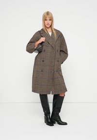 Houndstooth patterned oversized coat in brown and black, featuring a double-breasted design, wide lapels, and black knee-high boots.