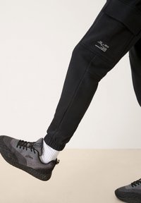 Svarta joggingbyxor med elastiska muddar, med sidofickor och logodetalj. Grå och svarta sneakers med texturerad design och snörning.