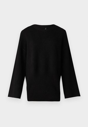 Melnā adīta džemperis ar plašu, apaļu izgriezumu, garām piedurknēm un ribotu apakšmalu. Tekstūra šķiet mīksta un nedaudz elastīga.