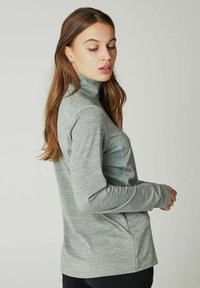 Lys grå, langærmet bluse med høj krave, struktureret stof og kontrasterende aqua syninger langs sømmene. Tætsiddende design med tommelhuller.