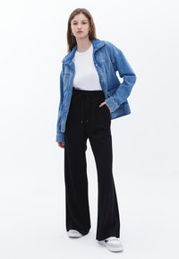 Giacca di jeans con una vestibilità rilassata, indossata sopra una t-shirt bianca. Abbinata a pantaloni larghi neri e sneakers bianche. Design semplice, look casual.