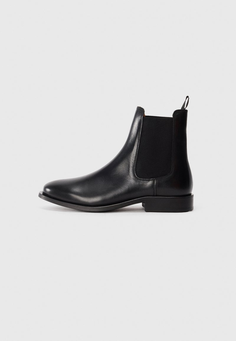 Botine Chelsea din piele neagră, cu panouri laterale elastice, vârf rotund, tab pentru tragere și toc joasă cu bloc. Textură netedă, cu detalii minime.