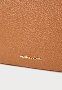 Tans gekorreld leer met een geprofileerde afwerking. Bevat een gouden 'MICHAEL KORS' logo dat aan de onderkant rechts is gegraveerd.